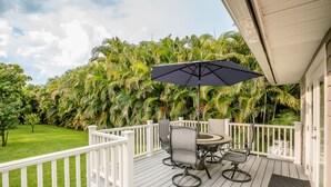 A deck with a table and chairs, surrounded by a white railing, overlooking a lush garden with palm trees.