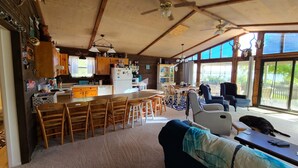 Una cocina amplia con armarios de madera y una isla central, un comedor con sillas de madera, y ventanas grandes que ofrecen vistas al exterior.