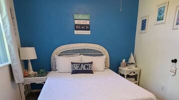 Une chambre à coucher avec un lit, un ventilateur de plafond, un panneau d’accueil, une petite table avec une lampe et un tapis.