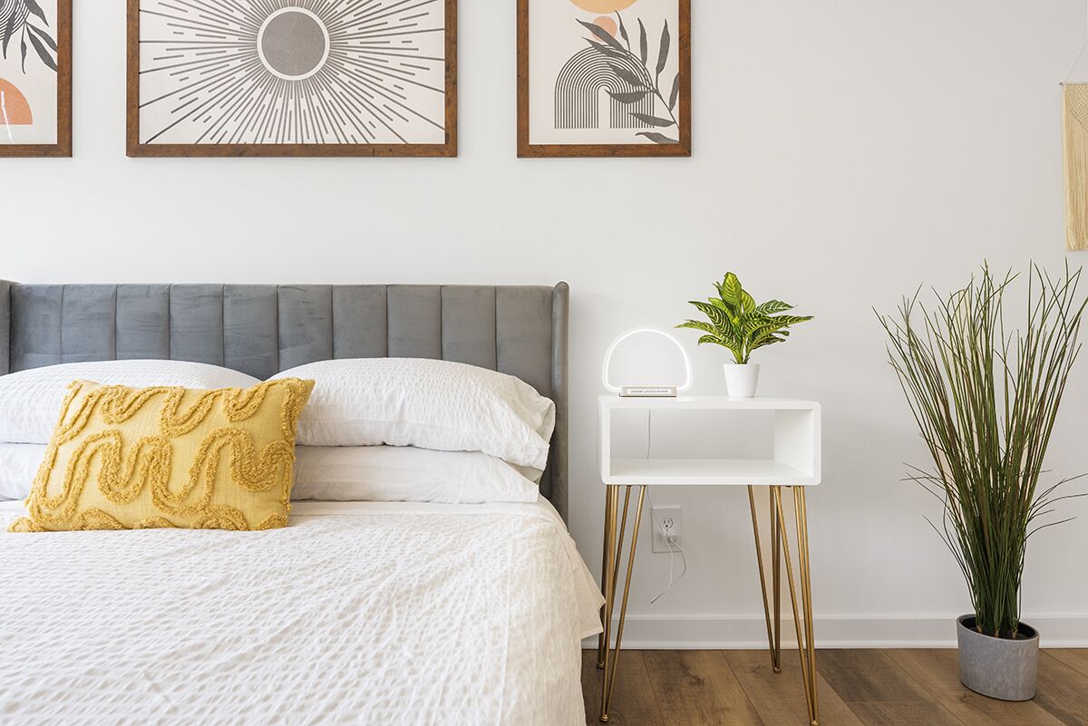 Un dormitorio ordenado con una cama, mesita de noche y una planta en maceta.