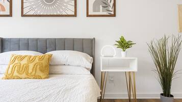 Un dormitorio ordenado con una cama, mesita de noche y una planta en maceta.