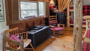 L’intérieur chaleureux d’un chalet avec un plancher en bois, une cheminée, un bureau avec un ordinateur et une fenêtre donnant sur les arbres.
