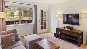 Ett vardagsrum med en soffa, ett soffbord, en tv på ett träställ och en skjutdörr i glas som leder ut till ett utomhusområde.