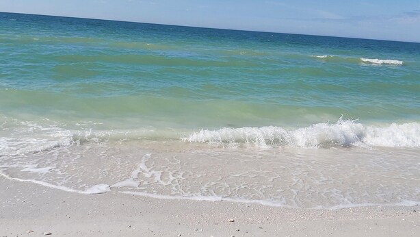 A beach with clear turquoise water and gentle waves. - Blind Pass Lagoon Unit 404 Boat Friendly, Pool, Close to it All! (Treasure Island)