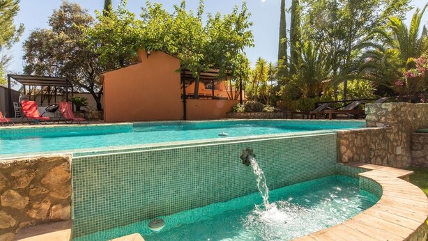 Una piscina amb una font, envoltada per una paret de pedra i un pont de fusta.