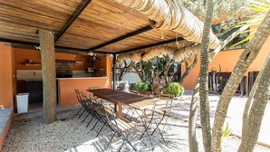 Un pati exterior amb taula i caires de fusta, envoltat d'arbres i una zona coberta amb teulada de gespa.