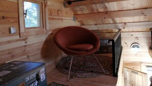 A wooden cabin interior with a red chair, a window, a radiator, and a small rug. - Lodge Domaine de kerolivier a bubble of tranquility with every comfort  (Plogonnec)