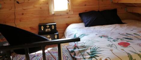 A wooden cabin bedroom with a bed, a small table, and a window.
