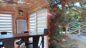 A wooden cabin with a dining area featuring a table and chairs, large windows, and a view of the surrounding forest. - Lodge Domaine de kerolivier a bubble of tranquility with every comfort  (Plogonnec)