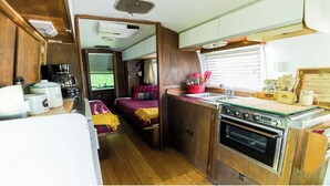 A compact RV kitchen with a stove, sink, and a small dining area with a bed.