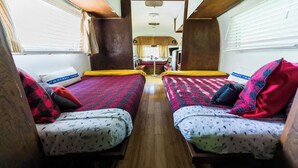 A narrow, well-lit interior with two beds, wooden walls, and a central table.