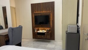 Quarto de hotel com cama, televisão, minibar e guarda-roupa.