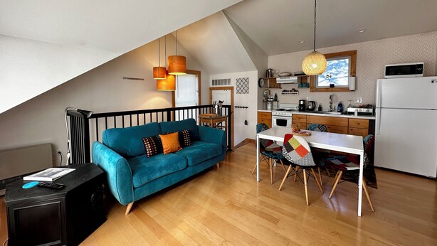 A cozy loft-style apartment with a blue sofa, wooden dining table, and a kitchen area.
