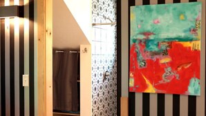 A bathroom with striped walls, a shower, and a colorful abstract painting.
