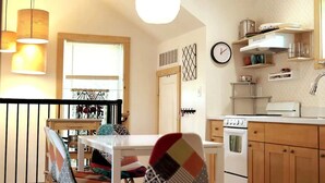 A compact kitchen with a stove, oven, and white cabinets. There is a dining table with chairs and a window with blinds.