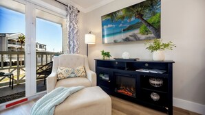 Ein Wohnzimmer mit Sofa, Kamin, einem großen Gemälde vom Strand und einem Balkon mit Blick auf Gebäude.