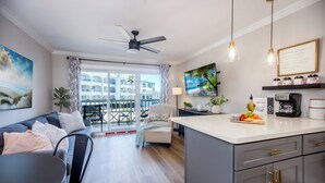 Ein modernes Wohnzimmer mit Sofa, Esstisch, Kücheninsel und einem Balkon mit Blick auf ein Gebäude.