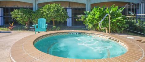 Un jacuzzi rodeado por una terraza con baldosas, con una silla y plantas cerca.