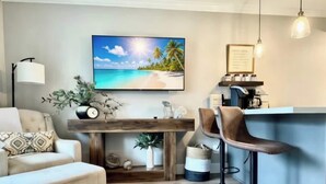 Ein Wohnzimmer mit einer Couch, einem Couchtisch, einem Fernseher, einer Bar mit Hockern und einem gerahmten Zertifikat an der Wand.