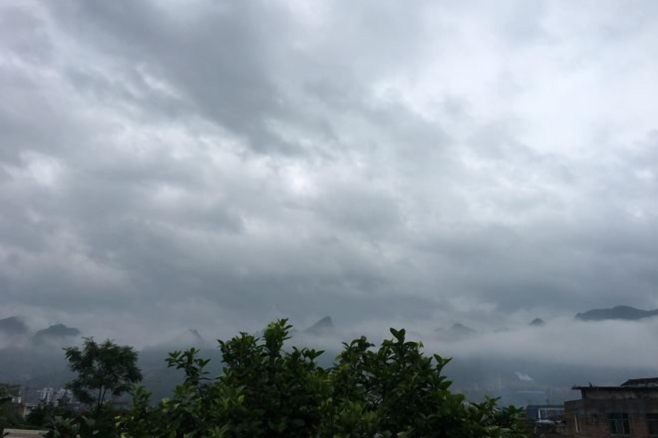 A cloudy sky with buildings and trees in the foreground.
