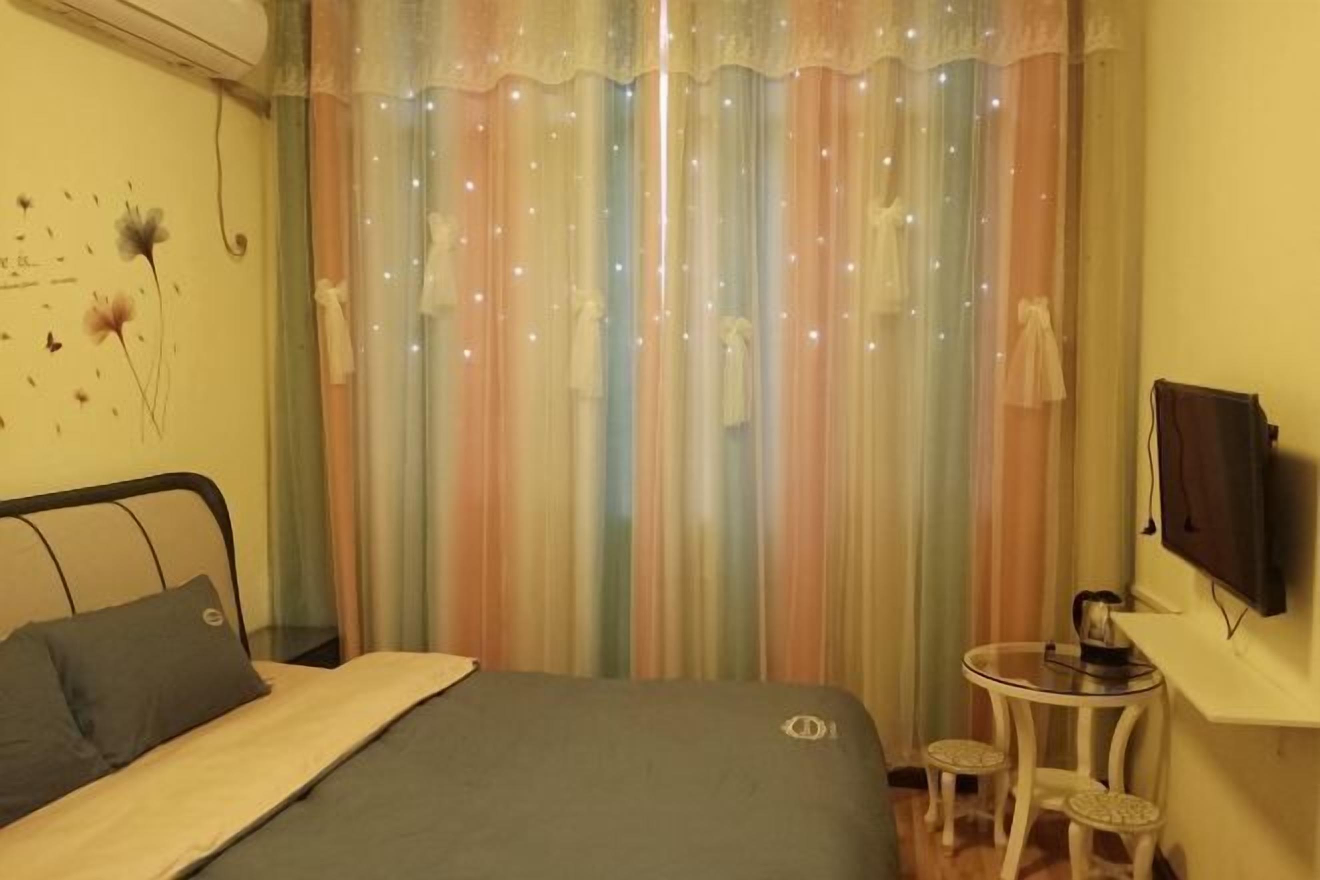 Ein Schlafzimmer mit einem Bett, einem kleinen Nachttisch, einem Fernseher und einem Vorhang mit hellen Verzierungen.