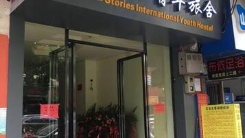 The entrance to a hostel with a glass door, a signboard with text, and a notice board with information.