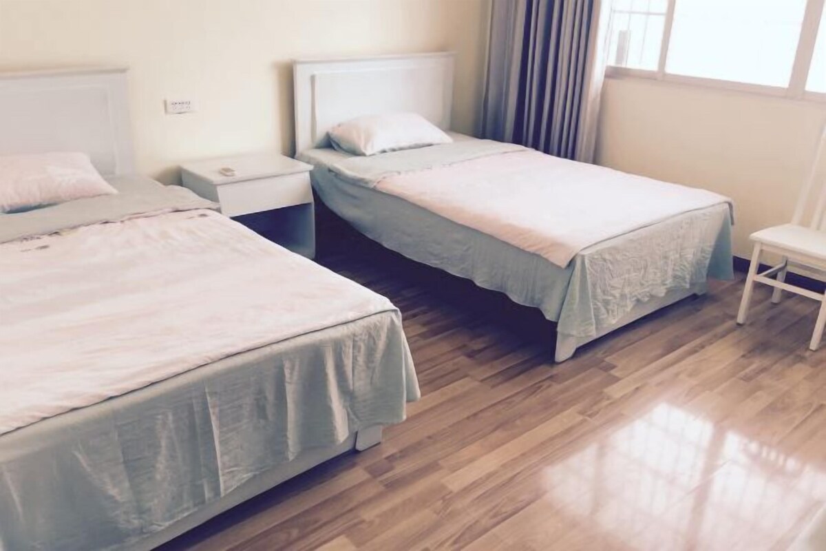 Quarto com duas camas de solteiro, uma mesa pequena e um banco.