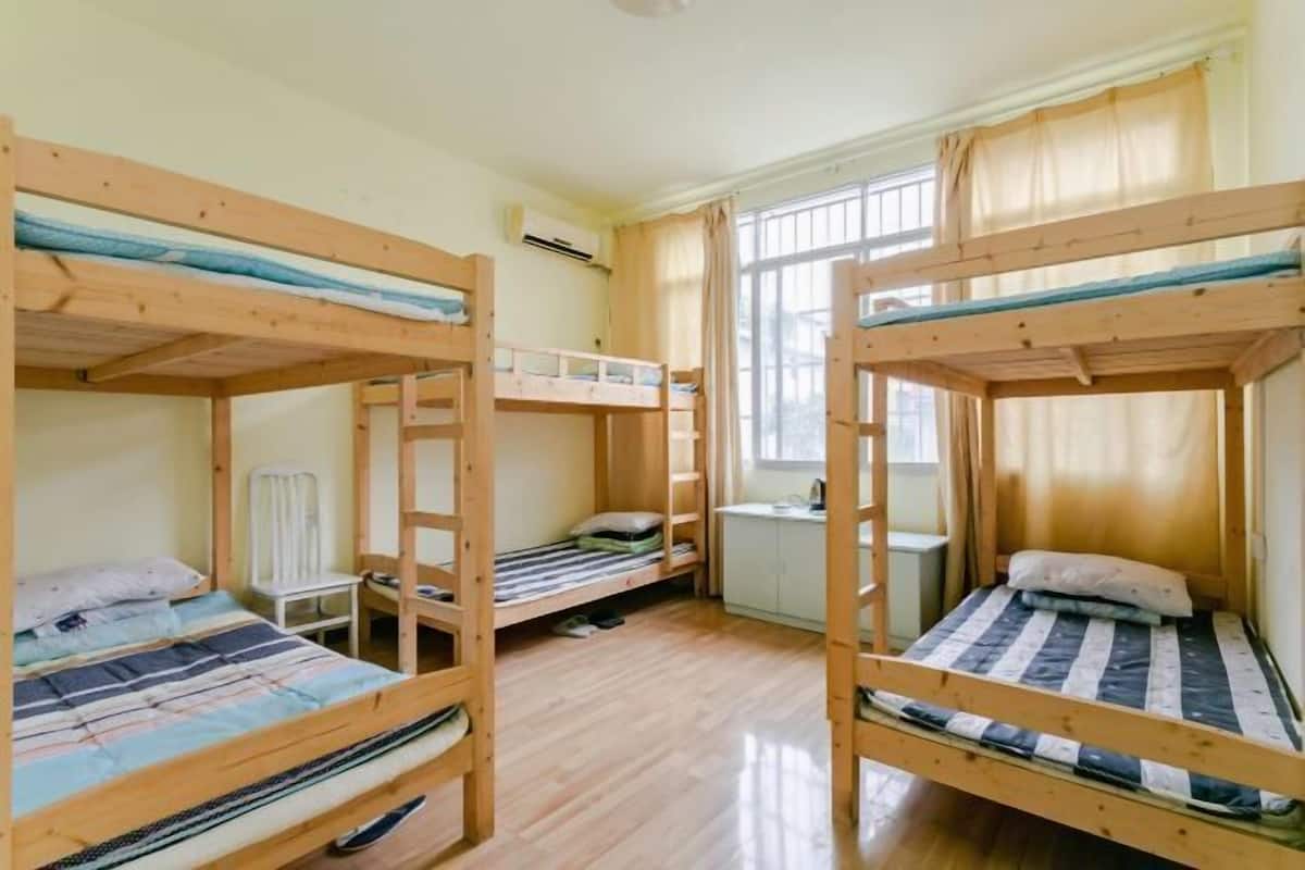 Una habitación con tres camas literas, un radiador blanco y una ventana con cortinas.