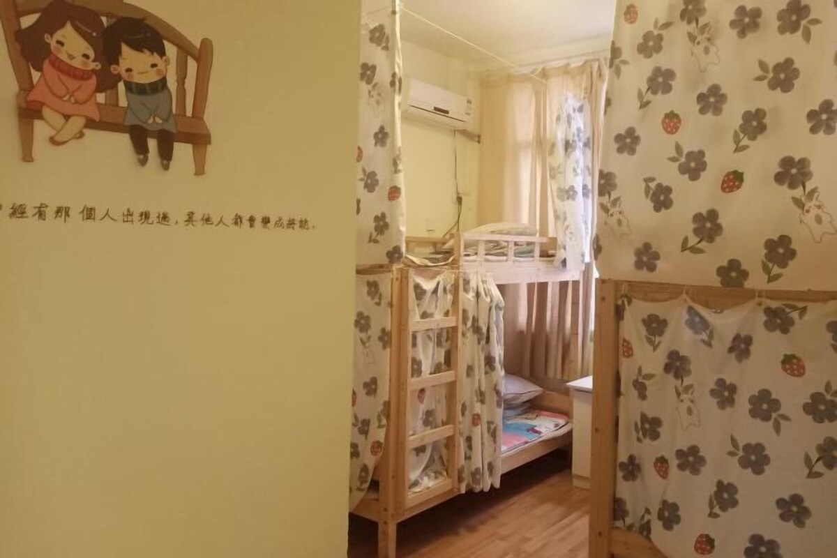 Quarto com cama de solteiro e bicama, cortinas florais, decoração de parede com duas crianças e cama com colcha estampada.