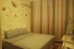Quarto com cama, ar-condicionado fixado na parede e janela com cortinas.