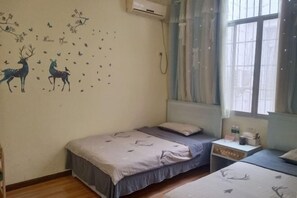 Quarto com duas camas, janela com cortinas, aparelho de ar condicionado e adesivos de parede com veados e borboletas.