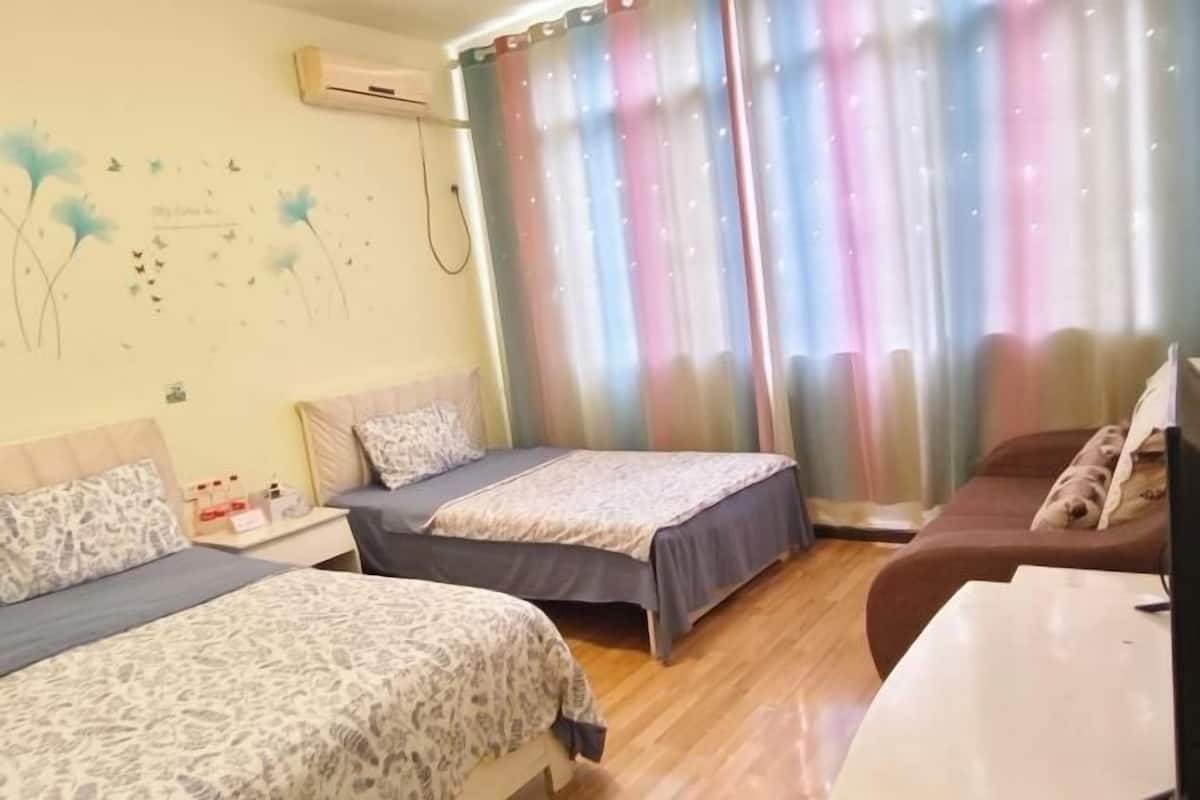 Habitación de hotel con dos camas, un sofá, una mesita y aire acondicionado instalado en la pared.