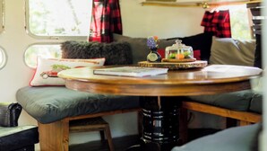 A cozy interior with a round wooden table, cushioned seating, a small decorative item on the table, and a window with curtains.