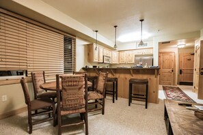 A kitchen with wooden cabinets, a microwave, and a refrigerator. There is a dining area with a table and chairs. - Quiet condo with free parking, pool, hot tub & sauna. 7 min walk to gondola.  (Park City)