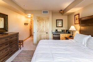 A hotel room with a large bed, a wooden dresser, a kitchenette, and a door leading to another room. - Quiet condo with free parking, pool, hot tub & sauna. 7 min walk to gondola.  (Park City)