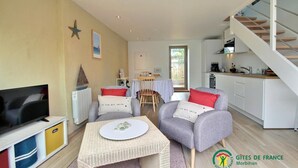 A modern living room with a TV, two armchairs, a small table, and a kitchen area with a staircase. - Steredeg - BADEN - Gîte (BADEN)