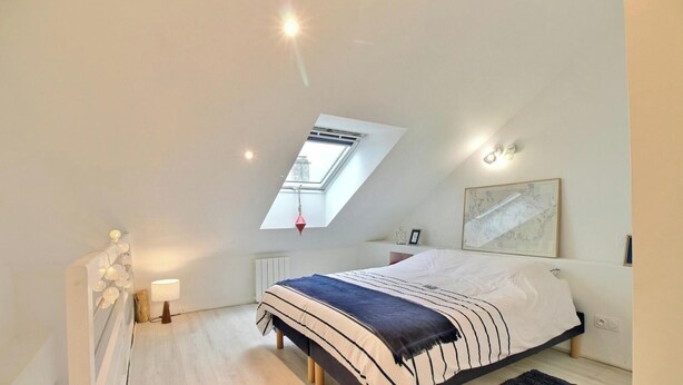 A bedroom with a skylight, a bed with striped bedding, a bedside table with a lamp, and a framed artwork on the wall. - Steredeg - BADEN - Gîte (BADEN)