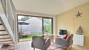 A modern living room with a large sliding glass door leading to a backyard. There is a TV, a small table, and two chairs. - Steredeg - BADEN - Gîte (BADEN)