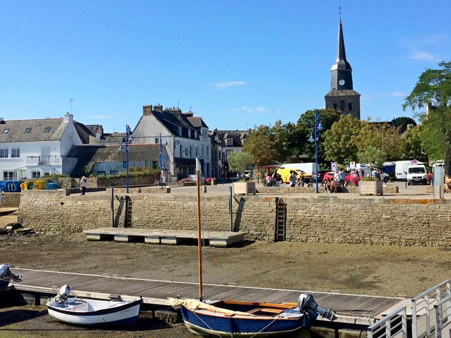 Un pueblo costero con muelle de piedra, barcos e iglesia con torre del reloj.