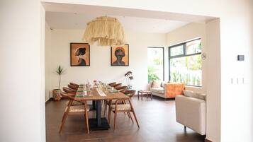 Un coin repas avec une table en bois dressée pour quatre personnes, entourée de chaises. Deux œuvres d’art encadrées ornent le mur, ainsi qu’un luminaire suspendu et une fenêtre donnant sur un paysage verdoyant.