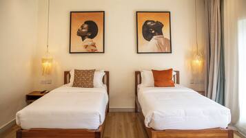 A hotel room with two single beds, wooden headboards, white bedding, and two framed portraits on the wall.