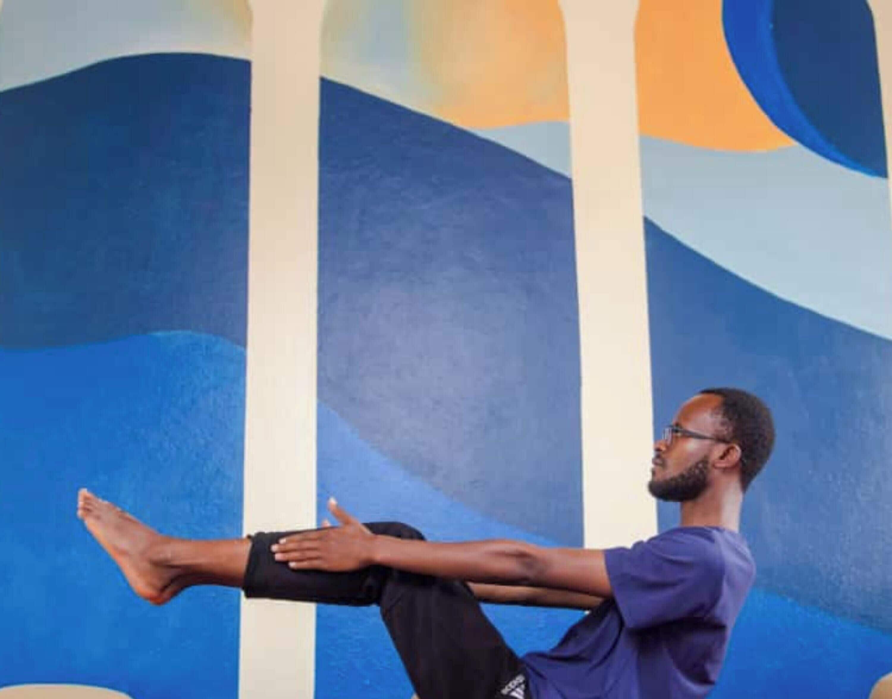 Una persona realiza un ejercicio de estiramiento frente a una pared con un mural abstracto azul y blanco.