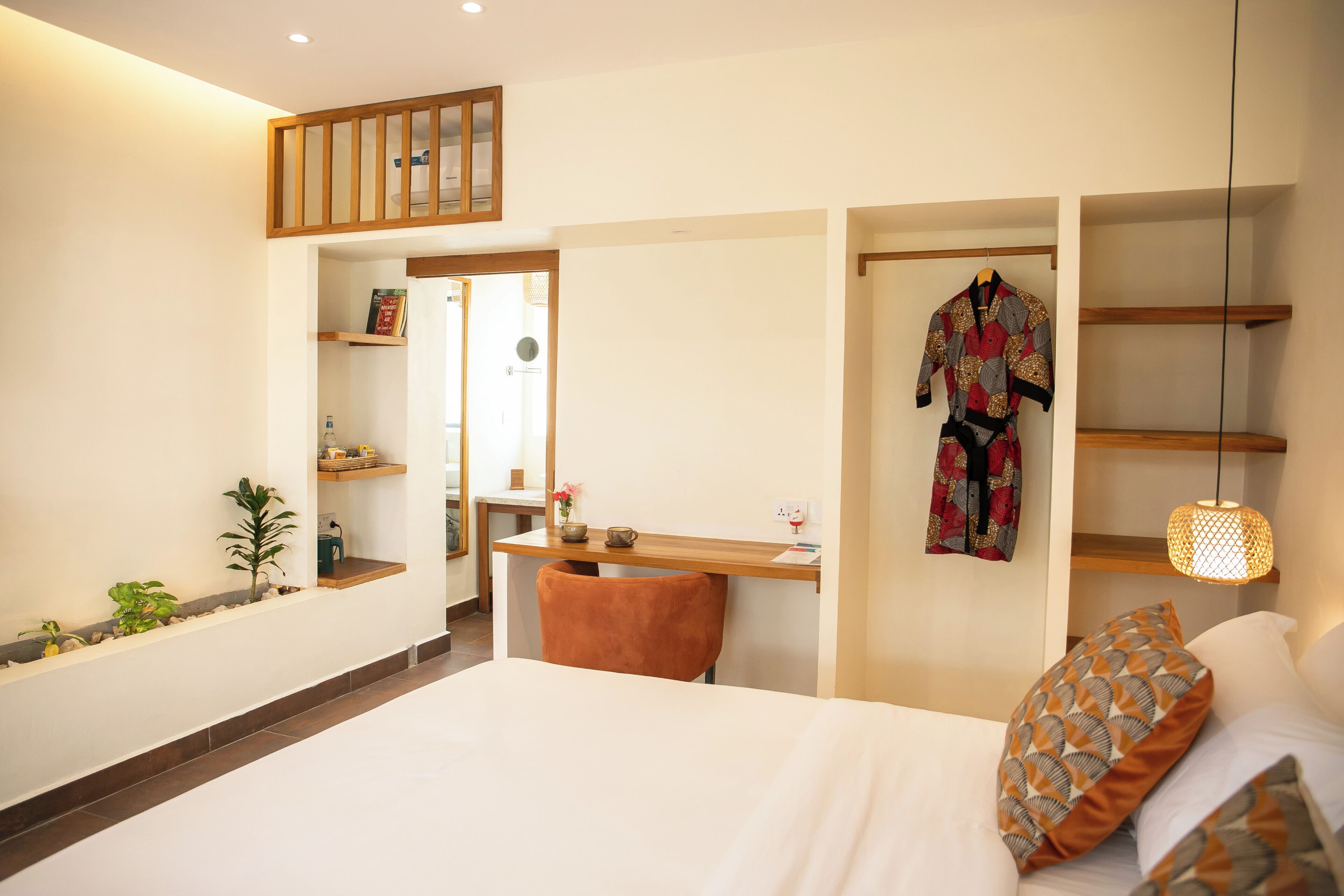 A hotel room with a bed, a desk, a chair, a wardrobe, and a hanging robe.