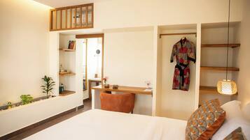 A hotel room with a bed, a desk, a chair, a wardrobe, and a hanging robe.