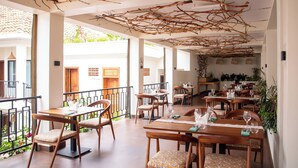 Un restaurante con mesas y sillas de madera, un techo con ramas y vistas al exterior.