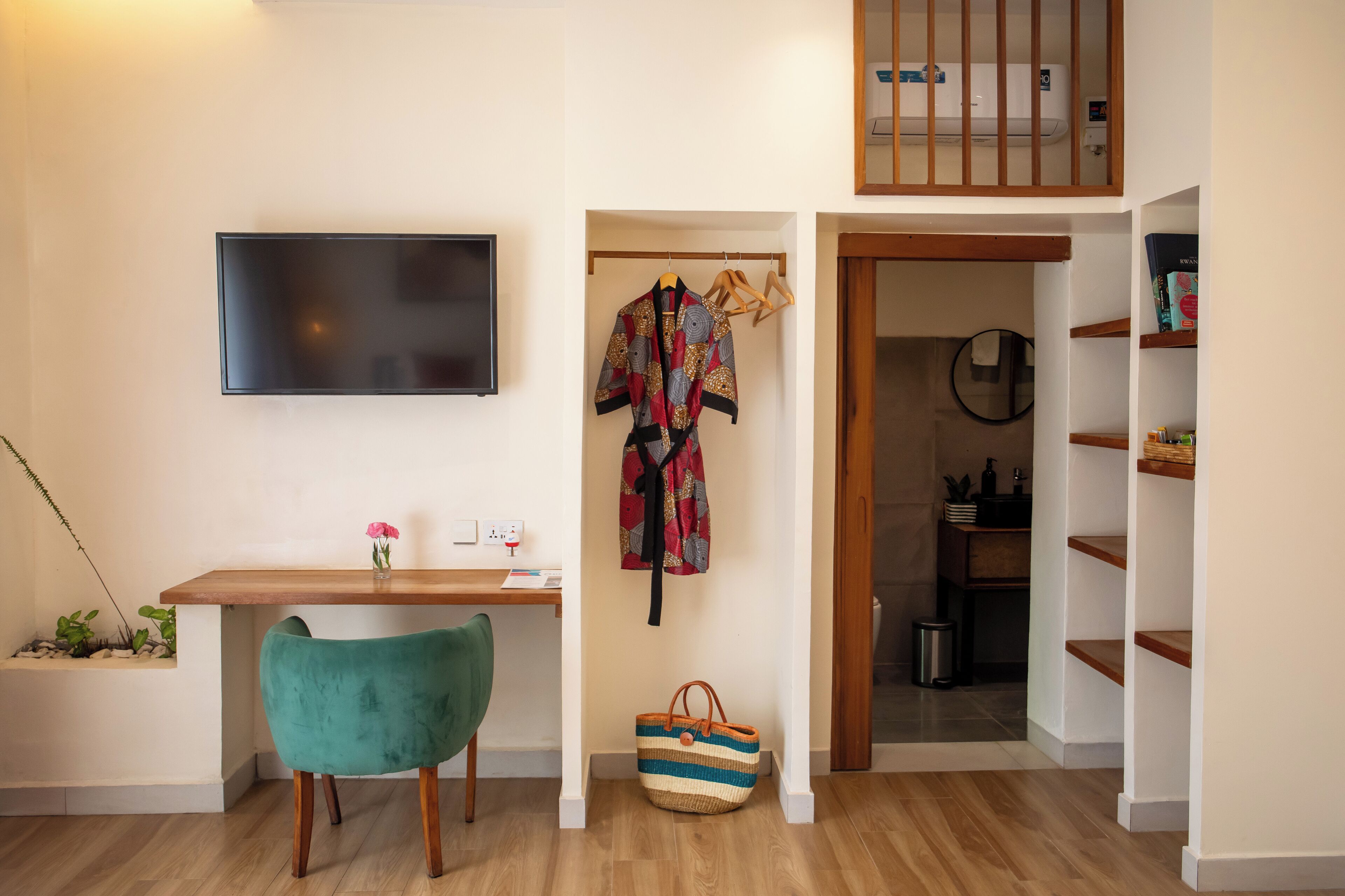 A modern room with a wooden desk, a teal chair, a hanging coat, and a striped bag.