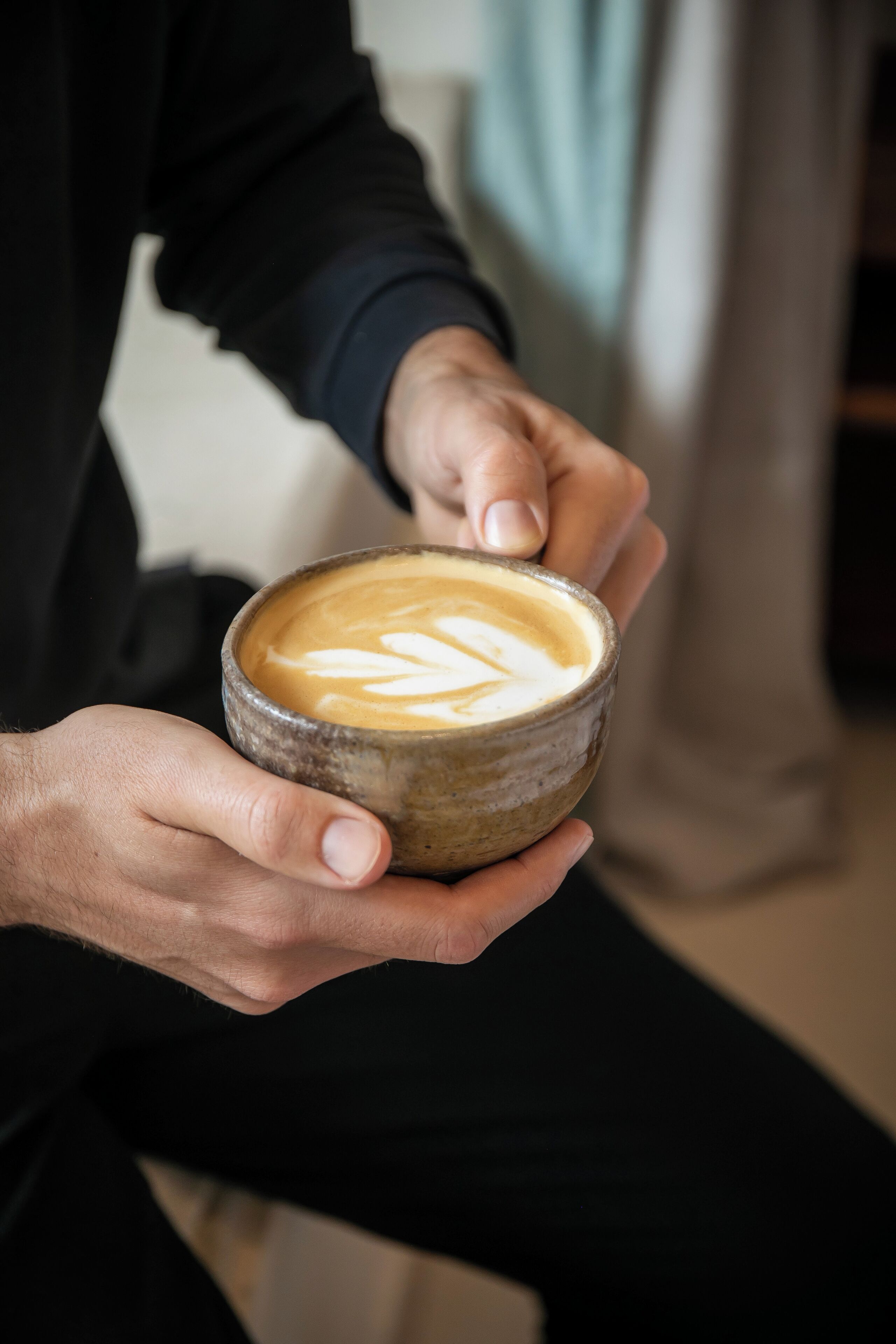 A person holding a ceramic cup with latte art.