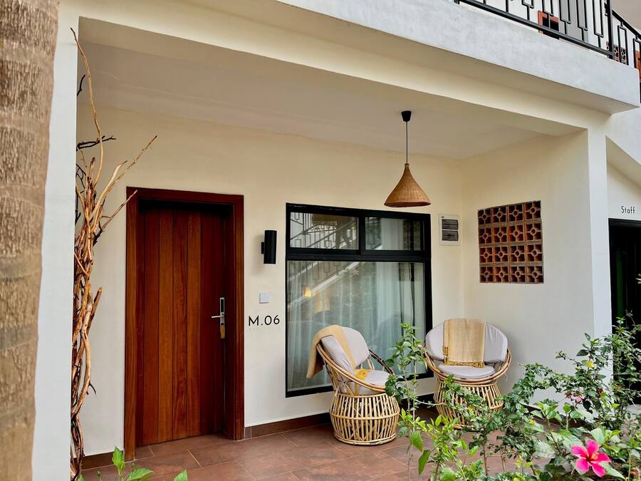 A modern entrance with a wooden door, two wicker chairs, a hanging pendant light, and a glass door with a view of the street.