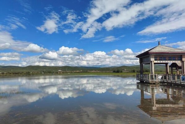 A clear reflection of a building on a calm body of water, with a clear sky and distant hills. - Hongyuan Xinyanyao Hotel (Hongyuan)