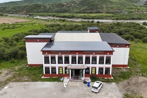 Un edificio con techo plano, entrada central y un estacionamiento con un coche blanco.